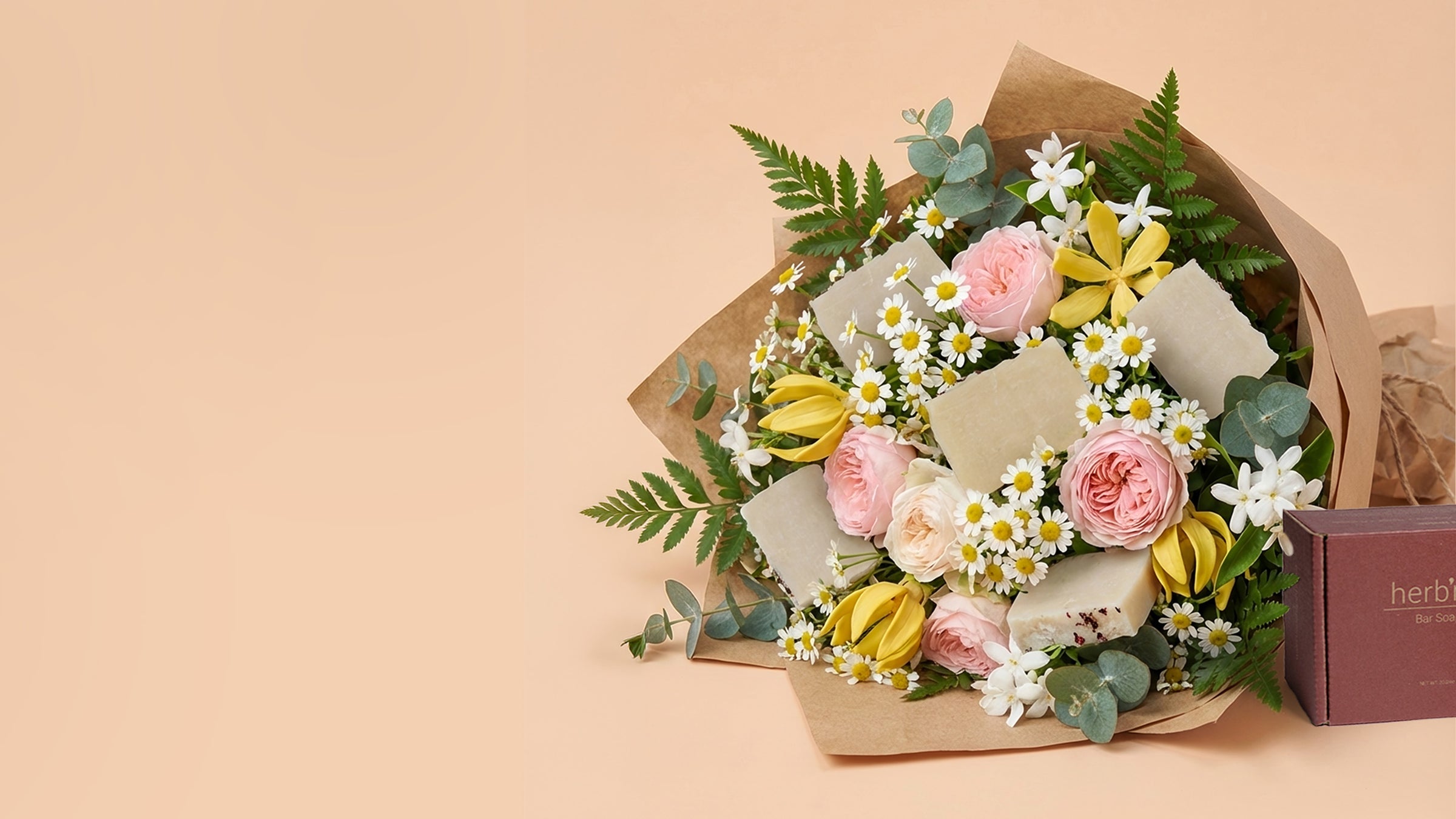 Bouquet of flowers that include bar soaps placed next to a gift box on a beige background